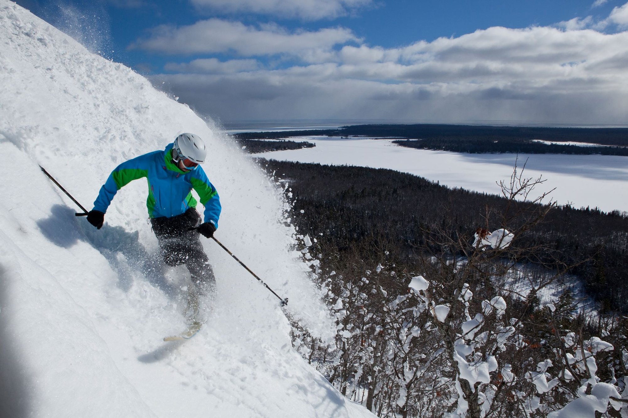 Skier carving down a steep run overlooking a frozen lake